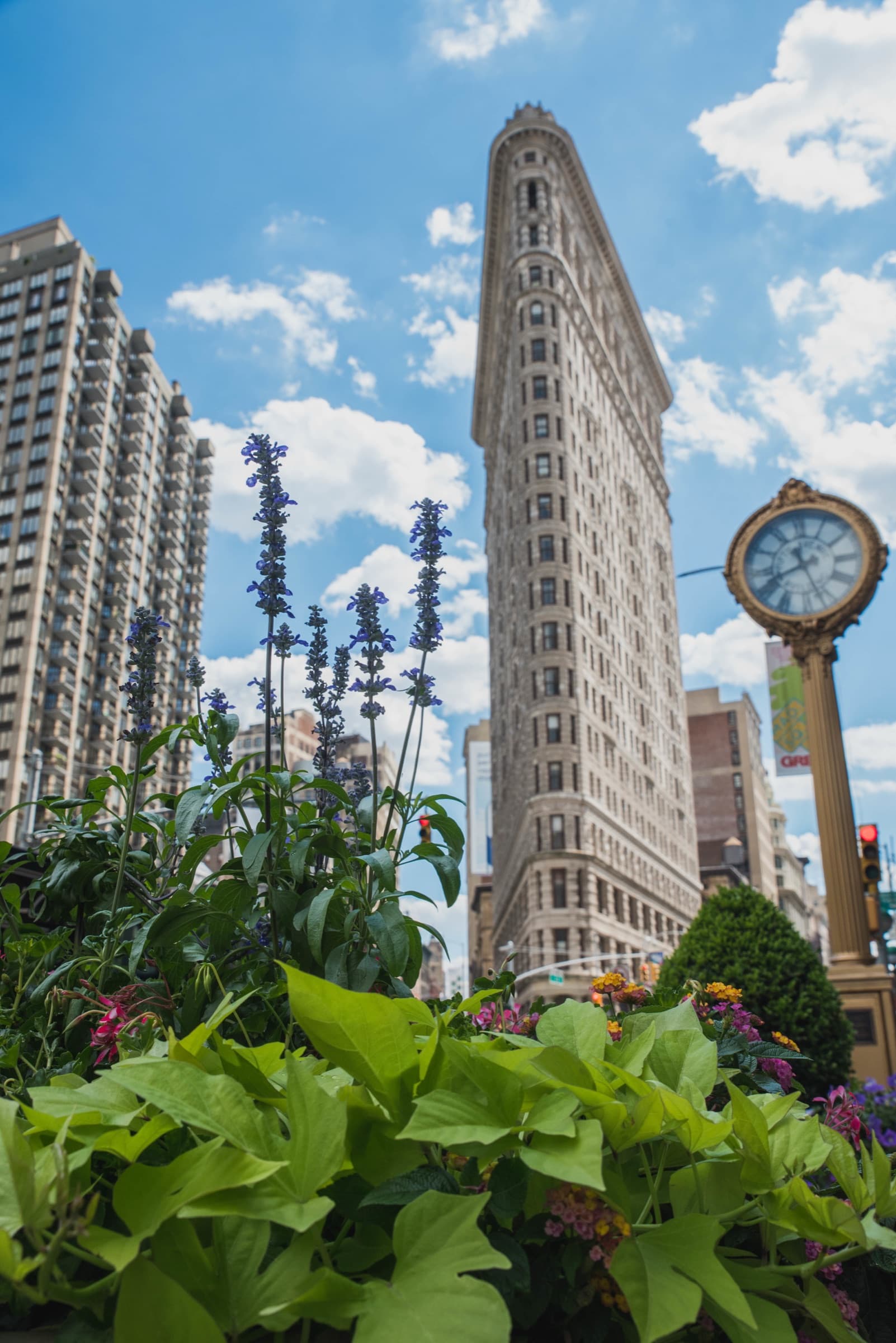The Flatiron Building in New York City with flowers and the gold Fifth Avenue clock